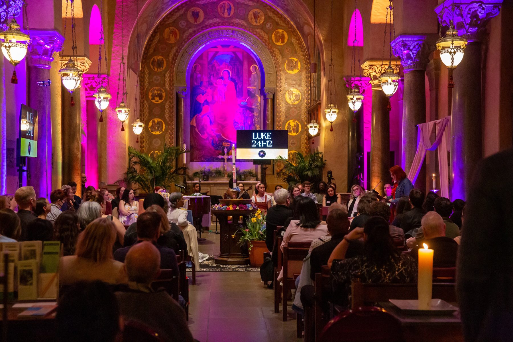 The congregation gathered in the nave under magenta light
